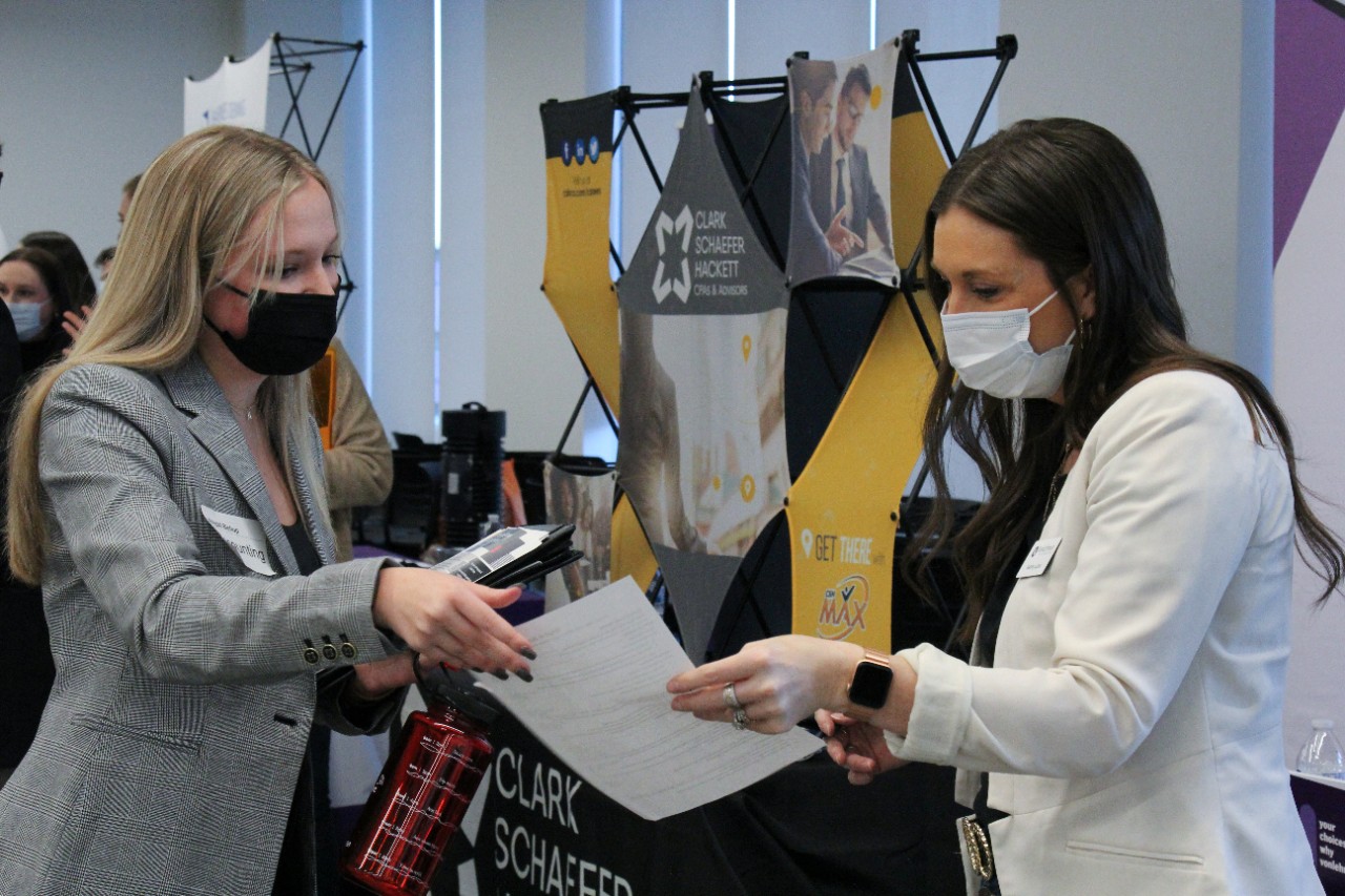 A woman in a gray jacket hands a piece of paper to a woman in a white jacket.