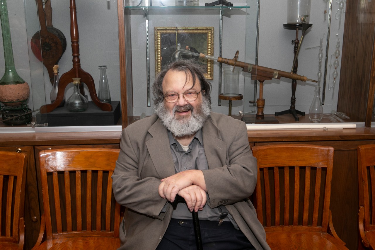 UC professor emeritus William Jensen sits in front of an exhibit in UC's chemistry museum.