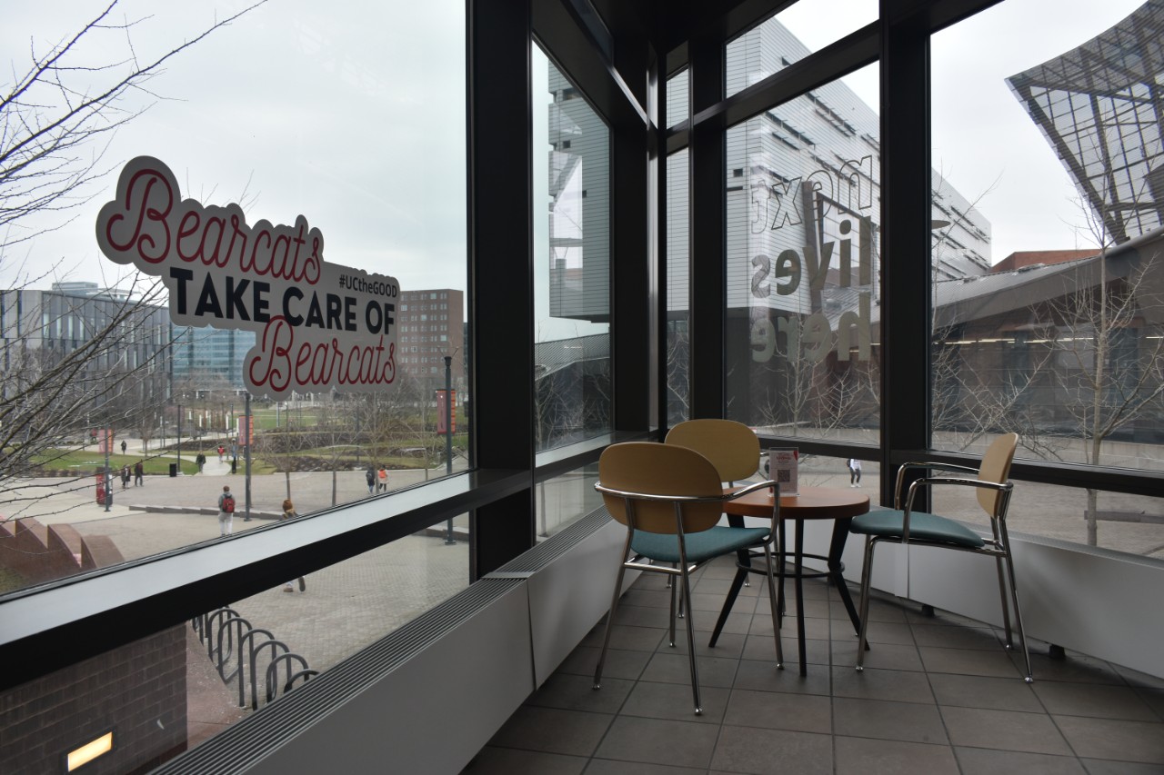 A small table and a sign reading "Bearcats take care of Bearcats" looking out a window toward UC MainStreet and Lindner College of Business