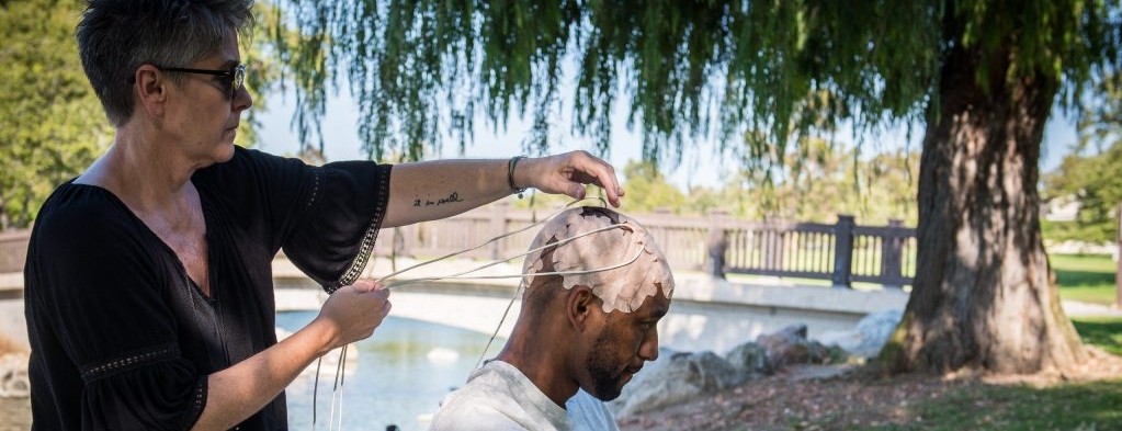 A woman applies electrical arrays to a male patient's head outdoors