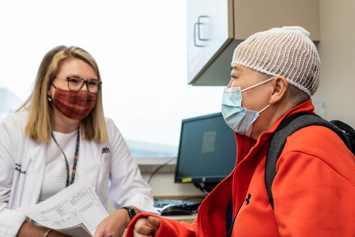 A woman wearing a lab coat talks with a patient wearing an Optune device