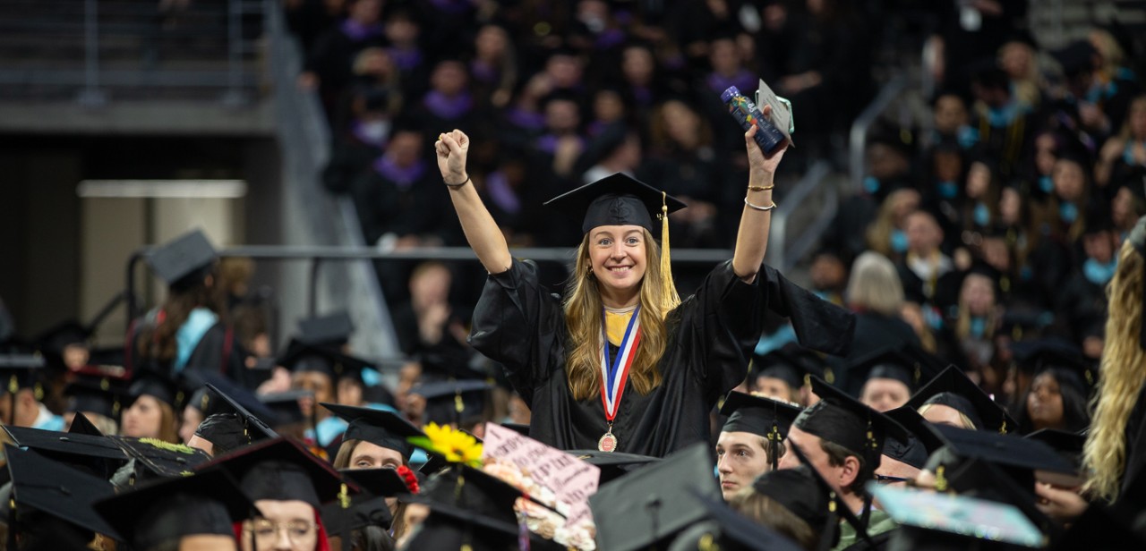 A UC grad raises her hands in jubilation on the floor of Fifth Third Arena.