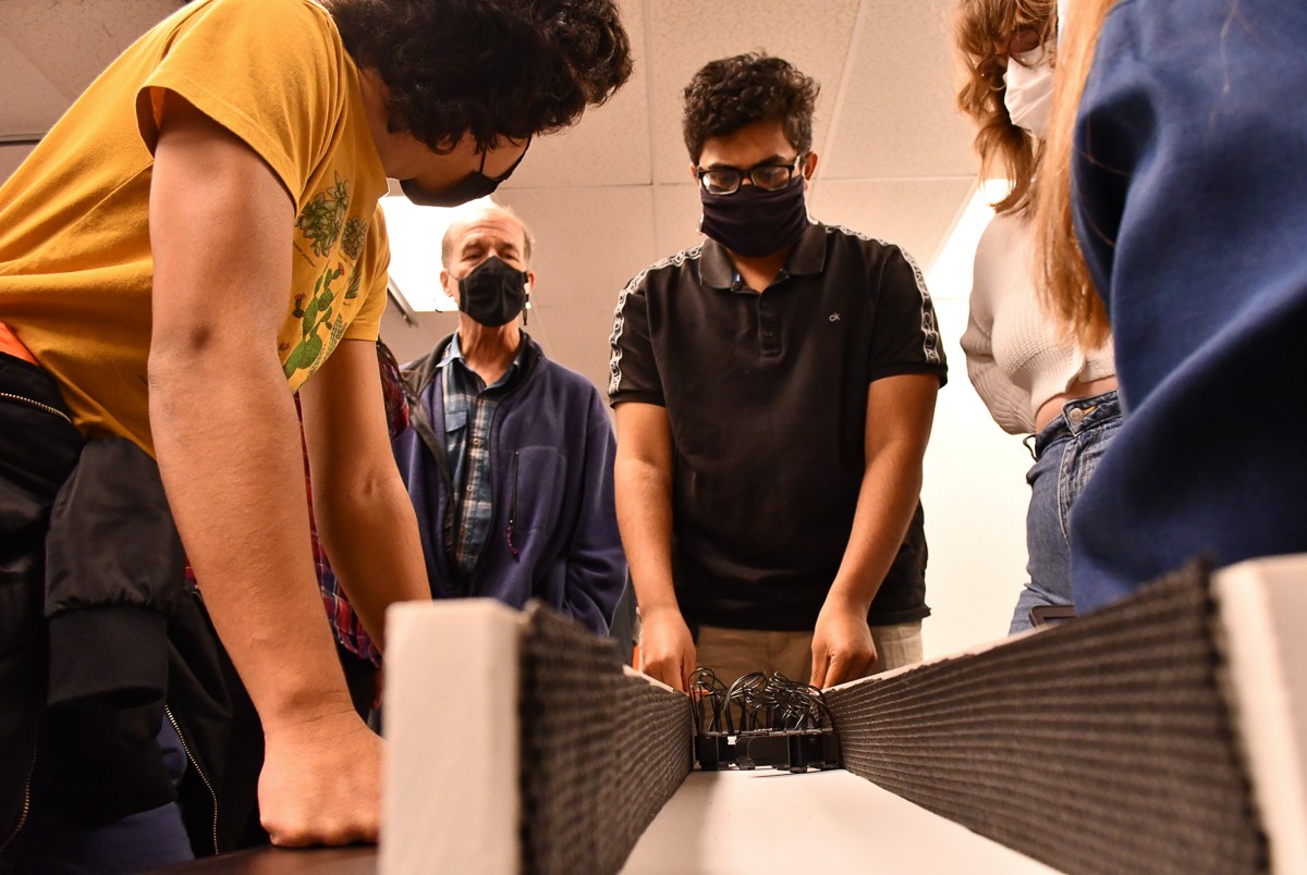 Students stand around a snake robot navigating a wooden obstacle course.
