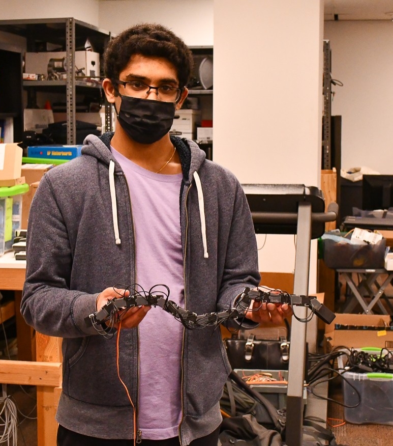 A student in a face mask holds up a robotic snake.