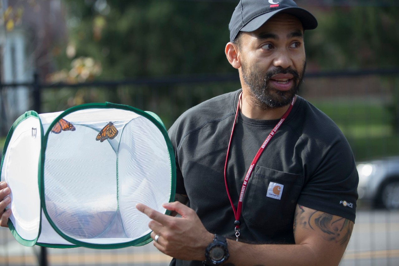 Patrick Guerra holds up a mesh container holding a butterfly,