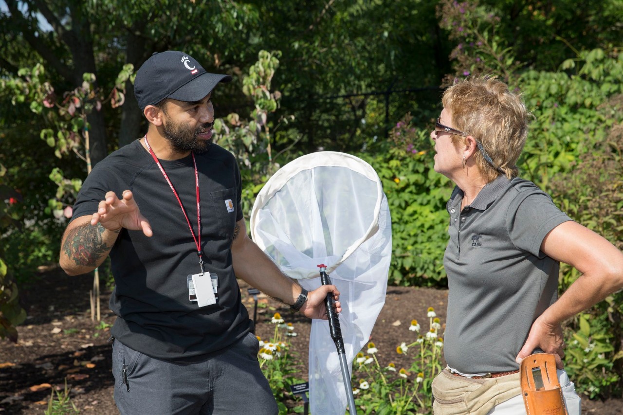 Patrick Guerra and Lyn Lutz talk in a garden full of flowers.