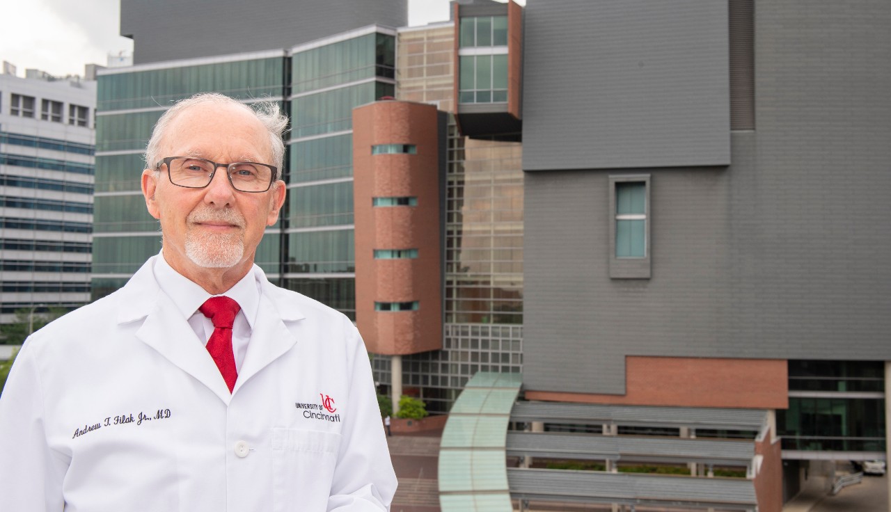 a man in a white lab coat with the UC College of Medicine in the background