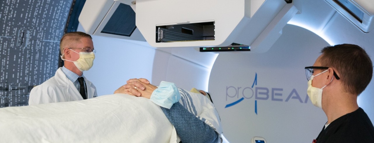 Medical staff stands while a patient lays in front of a proton treatment machine