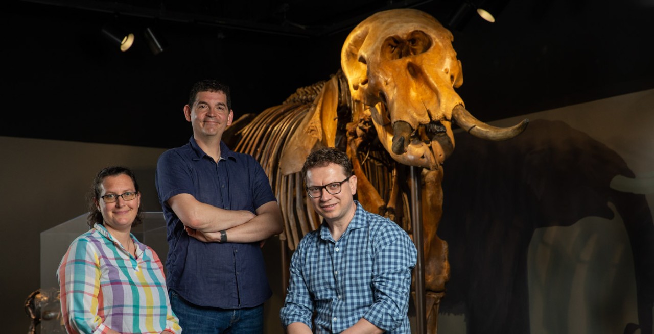 Brooke Crowley, Joshua Miller and Bledar Konomi pose in front of a fossilized mastodon skeleton at the Cincinnati Museum Center.