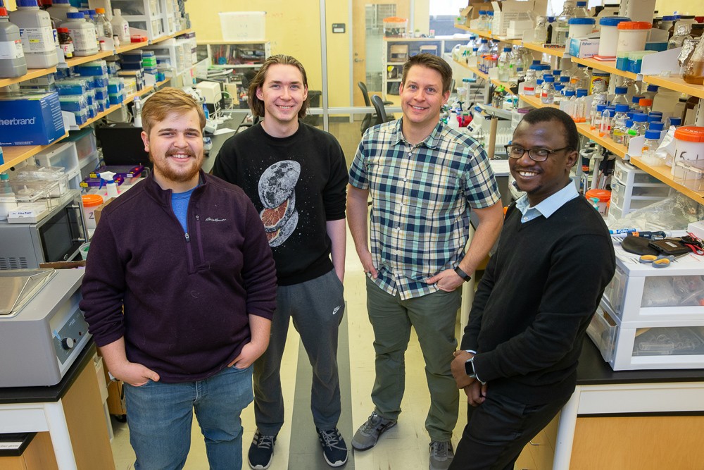 UC associate professor Joshua Benoit poses in his lab with three students.