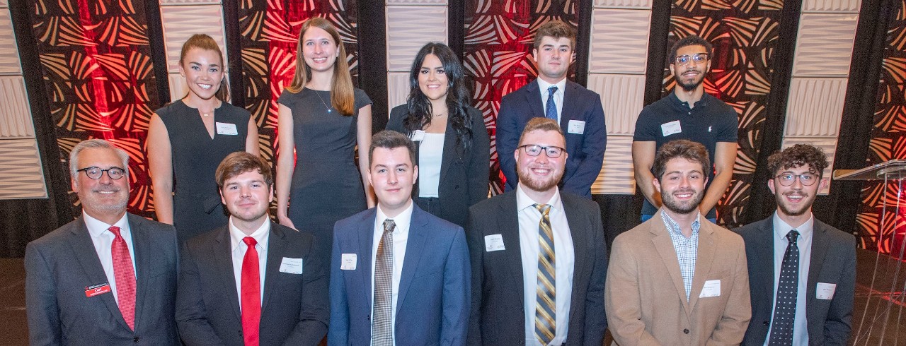 eleven people in business professional attire stand in two rows at the edge of am event stage