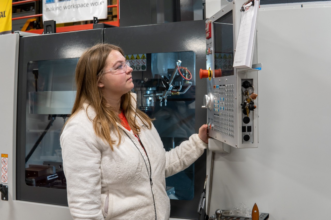 A student stands in front of a CNC machine in a manufacturing engineering lab.