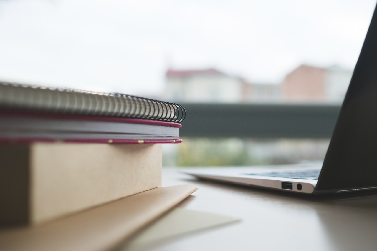 A stack of books sits next to a laptop.