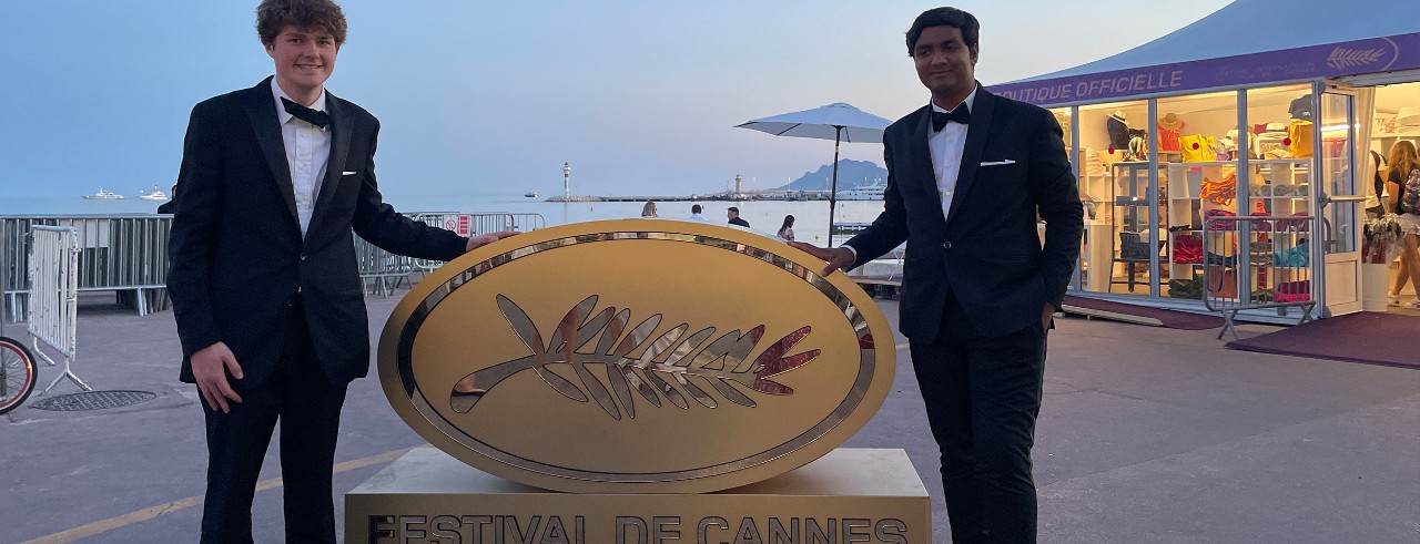 Tanmay Srivastava and a friend stand in front of a Cannes Film Festival sign.
