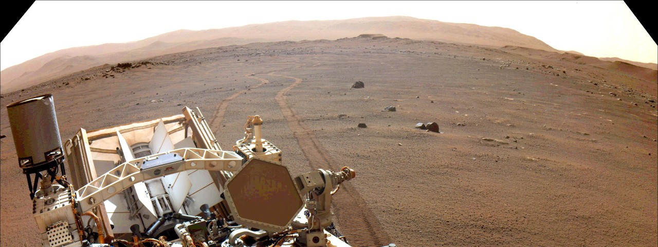 A view looking over Perseverance's body to its tracks in the Martian dirt. 