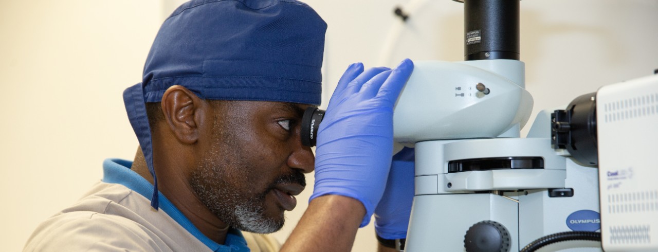 Dr. Hyacinth looks at a sample through a microscope in his lab