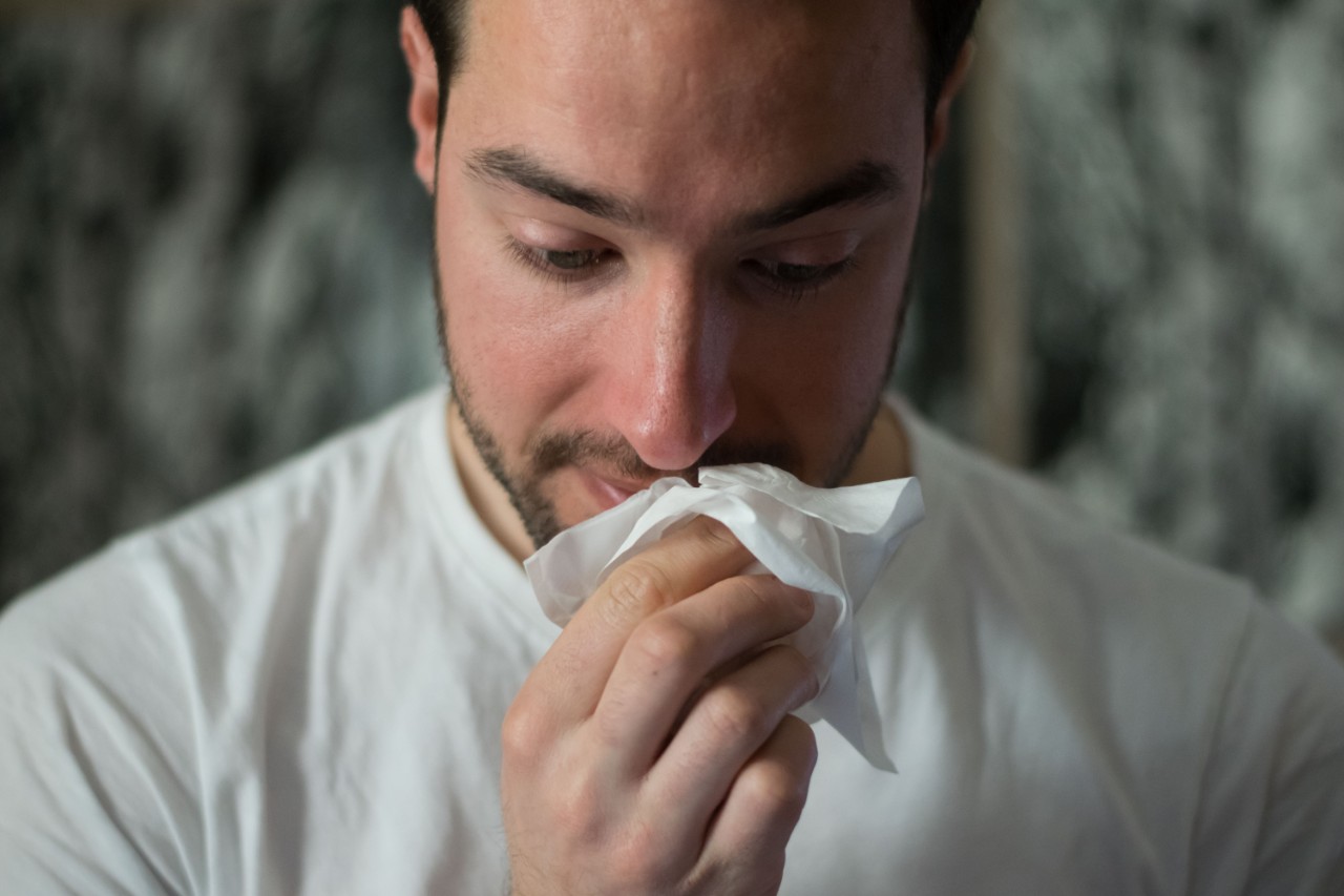A man holding a facial tissue sneezes