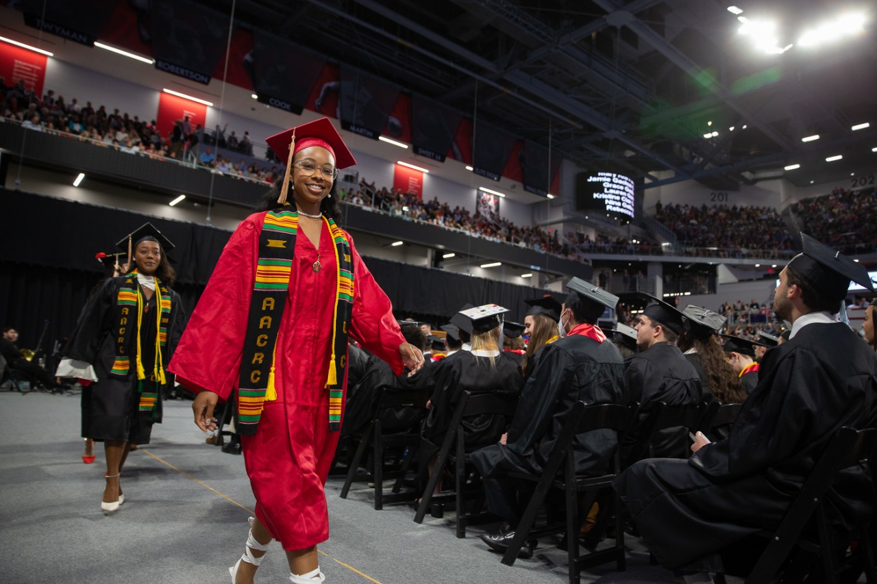 A graduate in a red cap and gown walks off the stage at Fifth Third Arena.