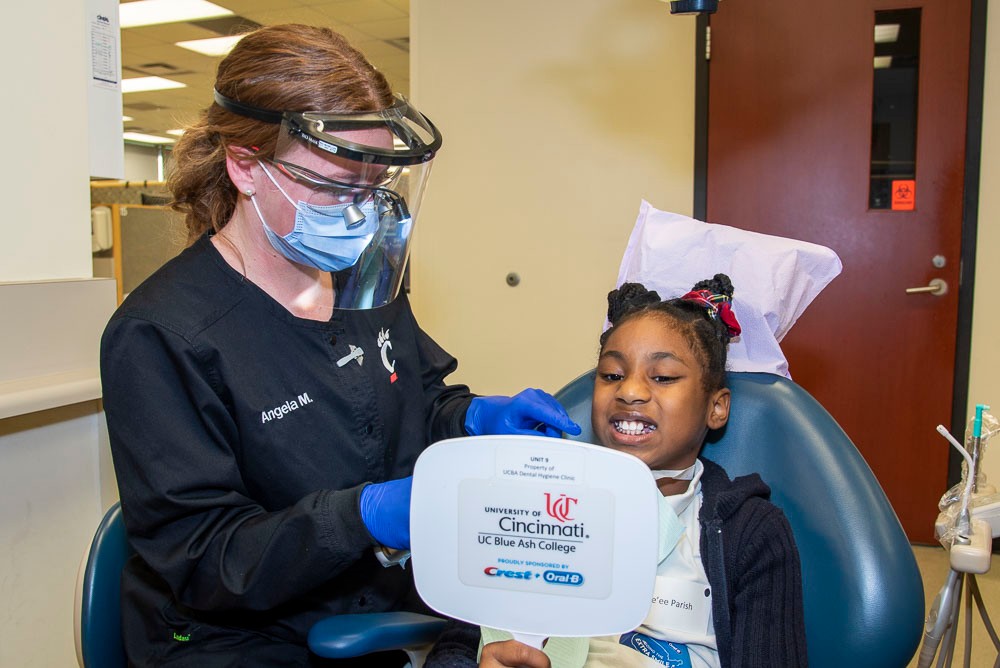 Masked dental hygienist inspecting teeth of smiling child