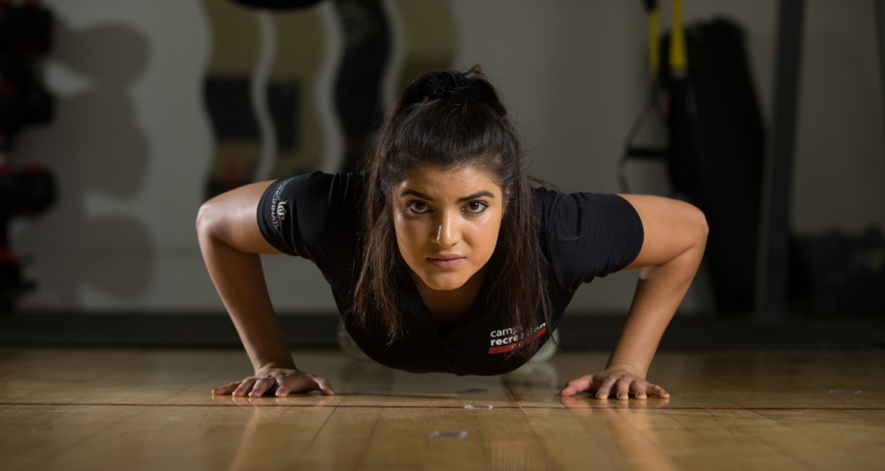 A UC student works out by doing pushups in a gym.