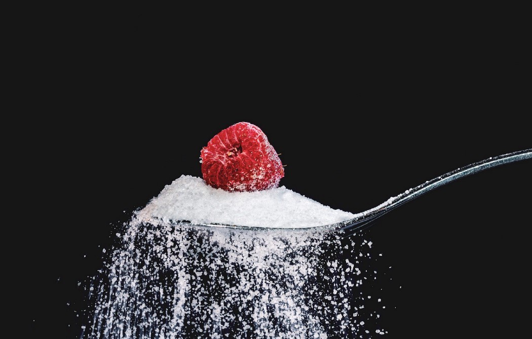 a spoon overflowing with artificial sweetener with a raspberry on top