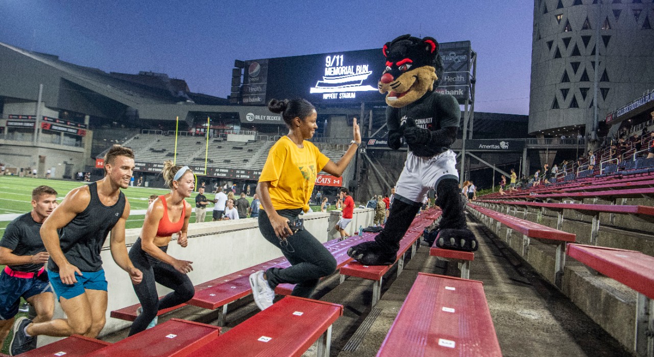 Runners give the UC Bearcat a high five while climbing the steps at Nippert Stadium.