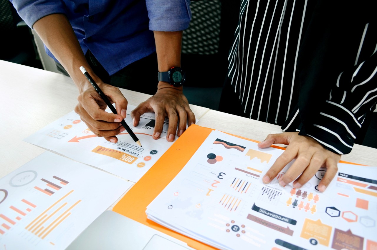 image of two people in an office setting looking at analysis papers.  Only the hands and lower body of the two individuals can be seen.