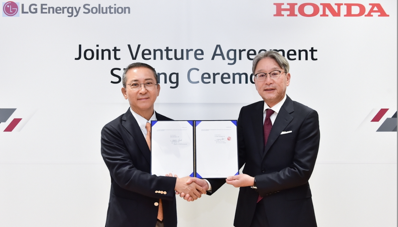 Executives from Honda and LG Energy Solutions shake hands while holding up a contract in front of a background with their company logos.