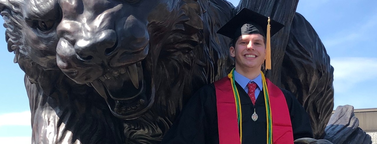 A college graduate in cap and gown poses with the Bearcat statue at the University of Cincinnati