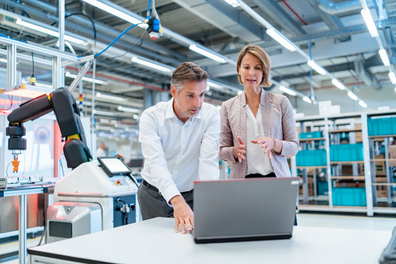 Businessman and businesswoman with laptop talking in a modern factory hall