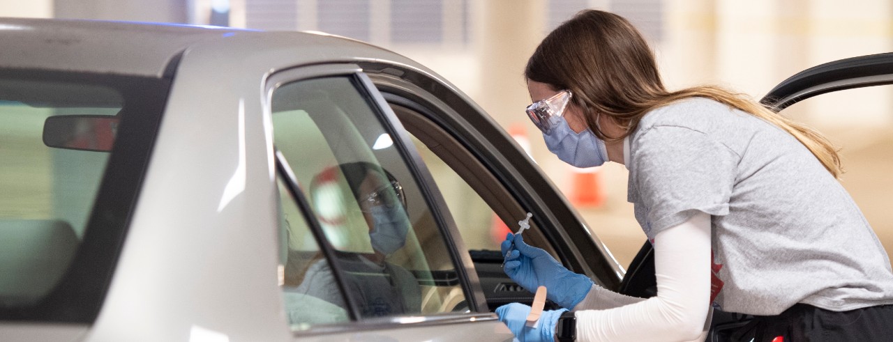 A UC College of Pharmacy student administers a COVID-19 vaccine to a patient in the passenger seat of a car during a drive-through clinic at UC Health.