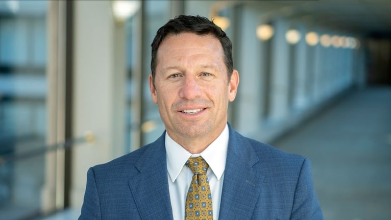 a man in a coat and tie smiles for the camera in a hallway