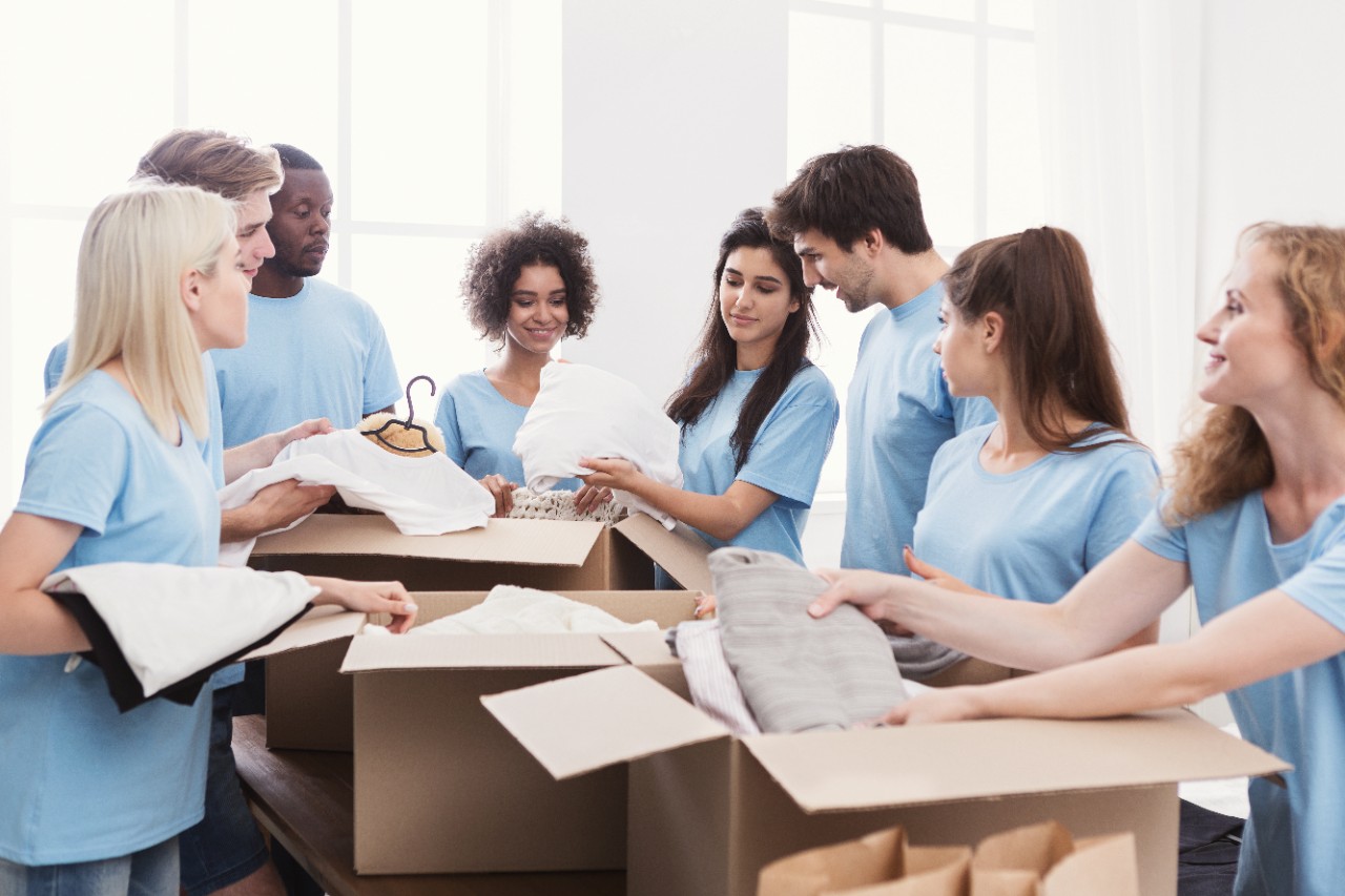 Young volunteers group sorting clothing donations in cardboard boxes, copy space