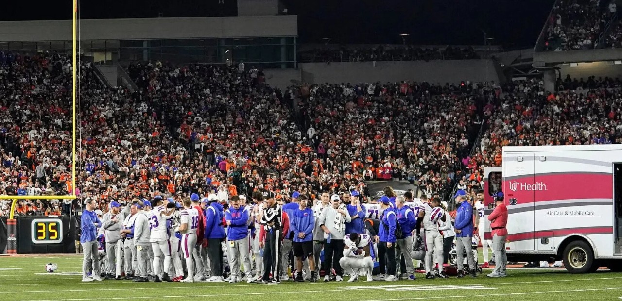 a group of football players, coaches and emergency medical personnel respond to an injured football player with an ambulance on a football field