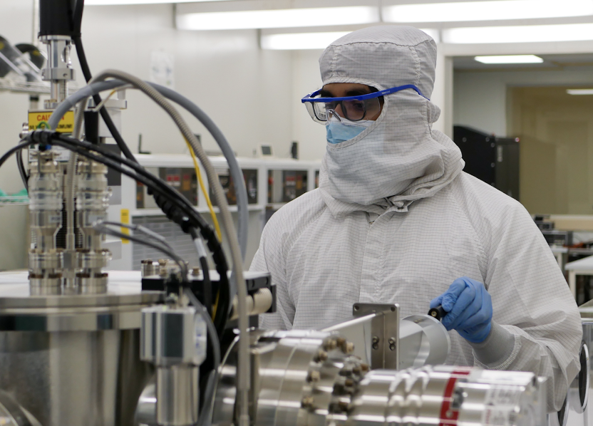 A student covered from head to toe in protective clothing works with stainless steel equipment in a cleanroom.