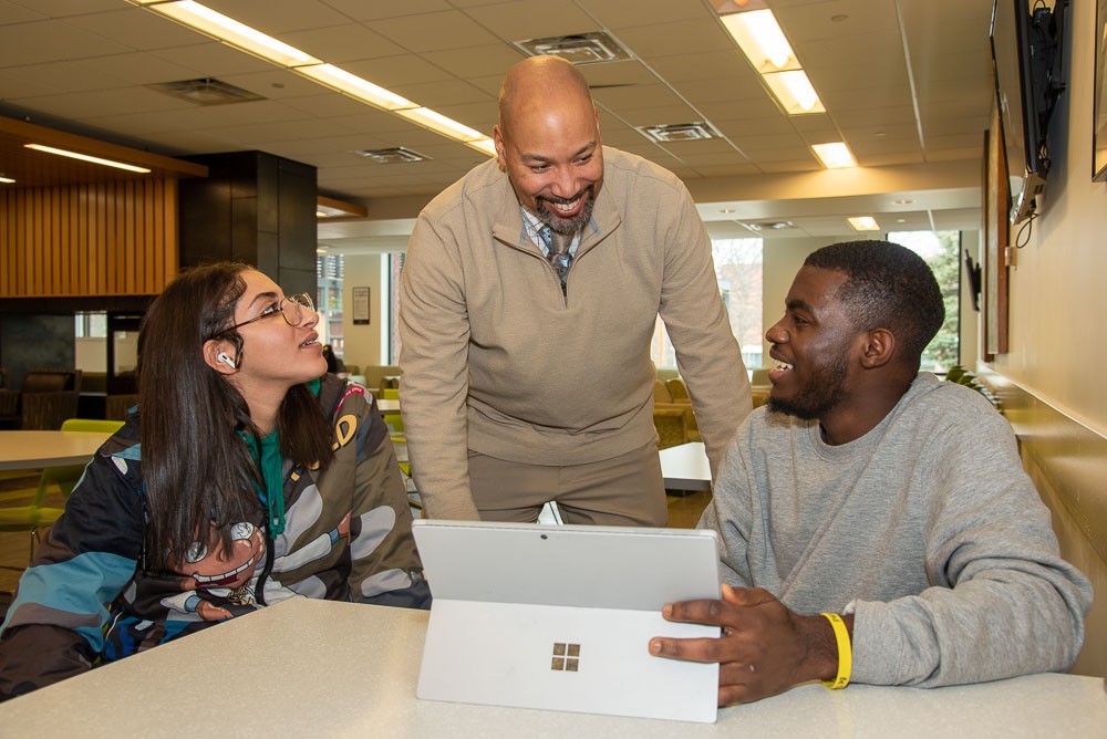 Bradford Mallory talks with two seated students in commons area