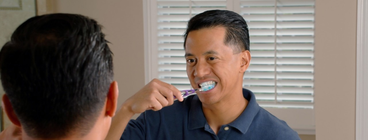 A man brushes his teeth while looking in a mirror