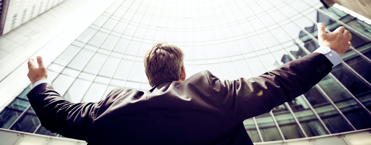 Back of man with arms spread wide in front of high-rise building.