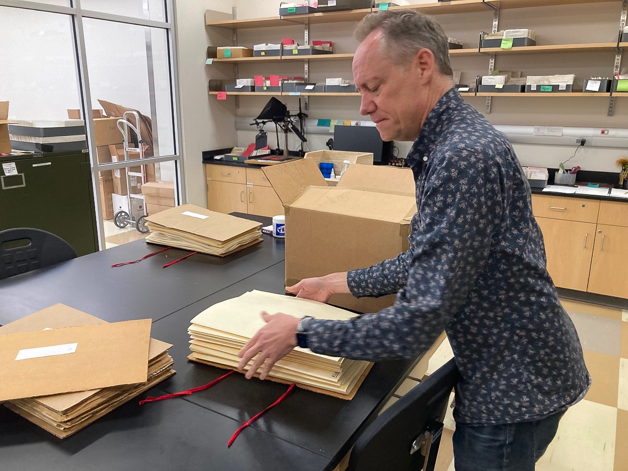 Eric Tepe unpacks manila folders from a cardboard box in a biology lab. 