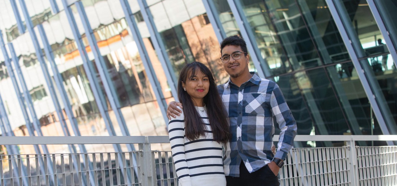 A couple poses together in front of a window reflecting UC's Main Street.