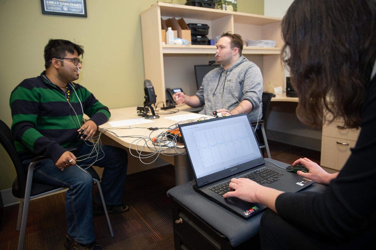 Two students hooked up to sensors have a conversation while a professor monitors their physiology on a computer screen.