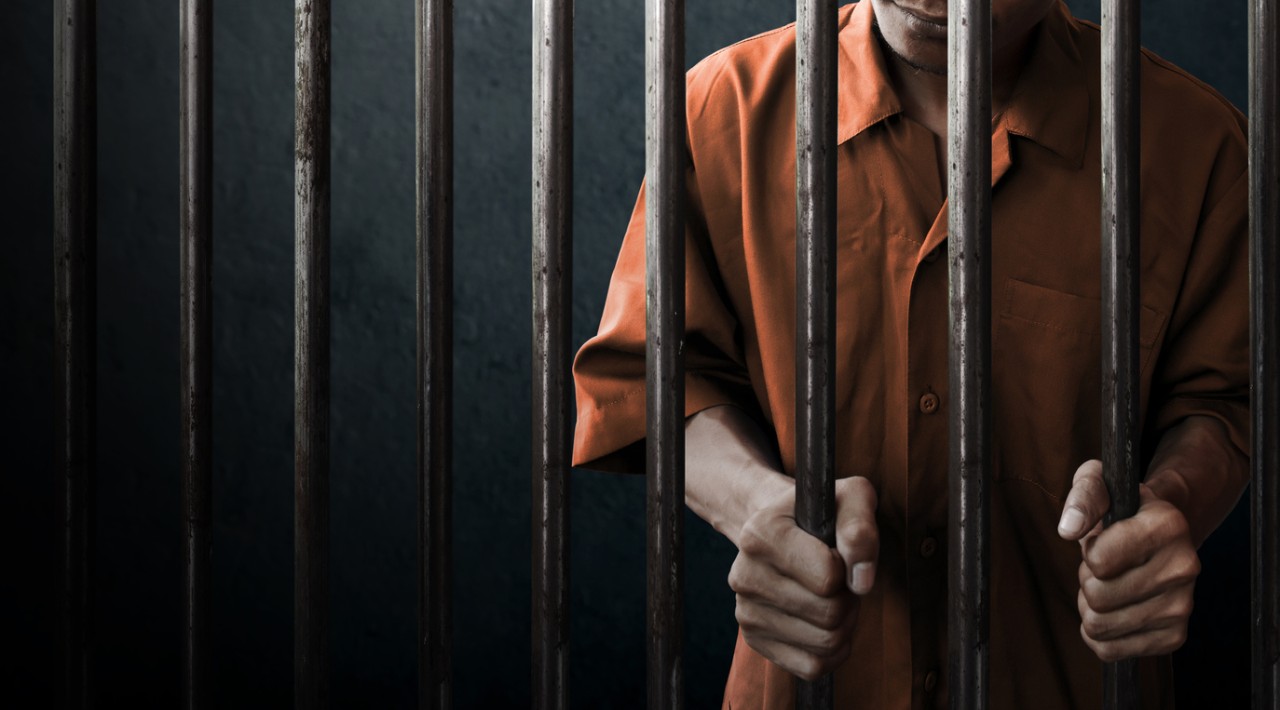 Man standing behind prison bars dressed in orange outfit
