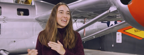 Engineering student Lynn Pickering gestures and smiles in front of an airplane. 