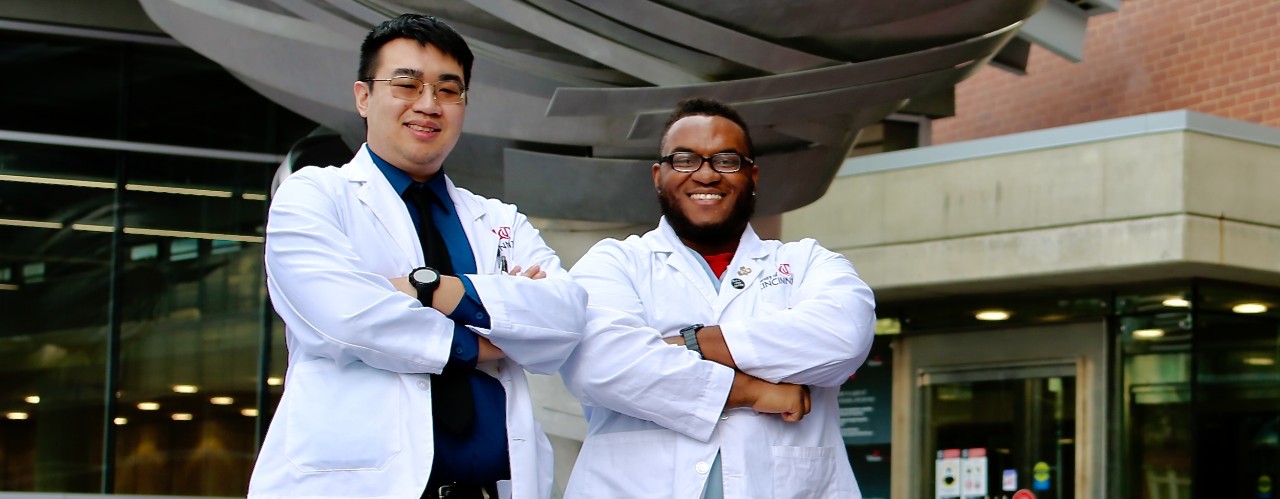 UC med students Minh Nguyen and William Smith stand in front of UC's College of Medicine building on Eden Avenue.