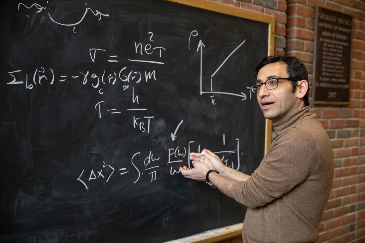 UC theoretical physicist Yashar Komijani stands at a blackboard writing equations.