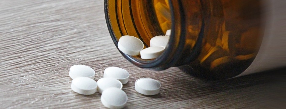 A pill bottle spilling white pills over a counter.