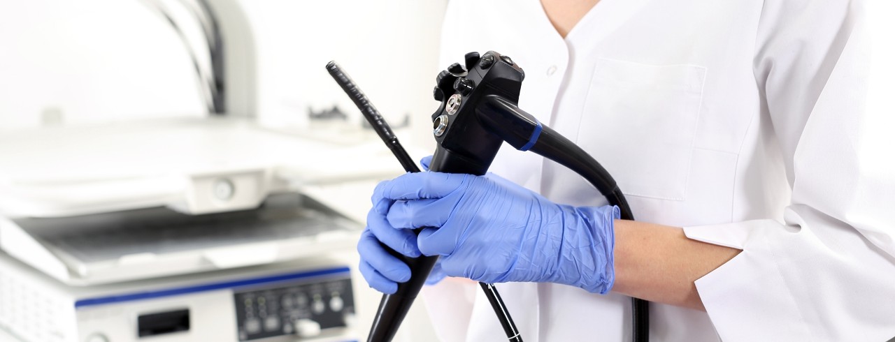 A technician wearing gloves holds a colonoscopy scope