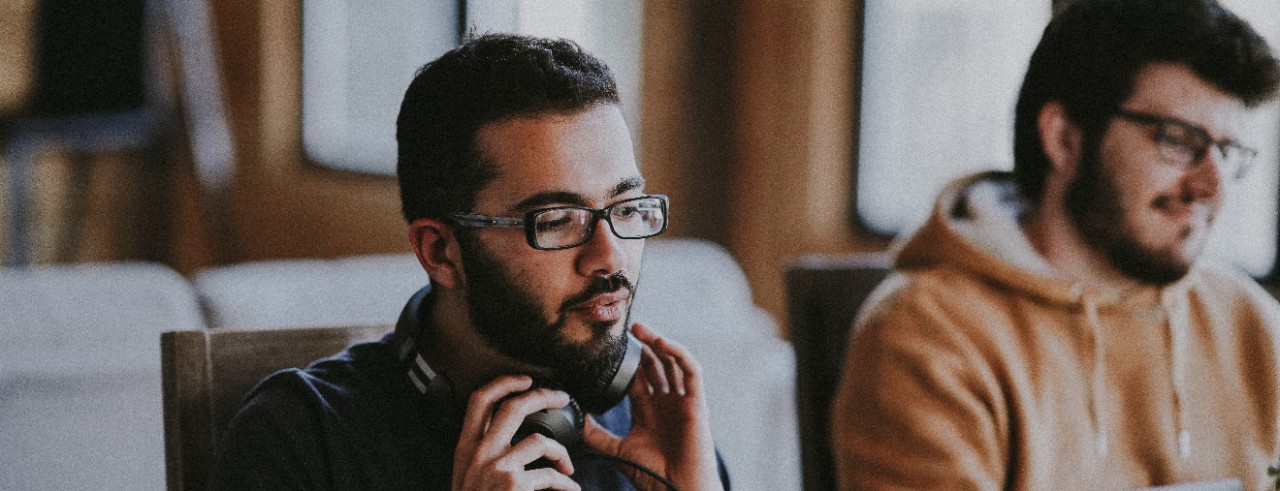 Two men sit at a desk working on laptops