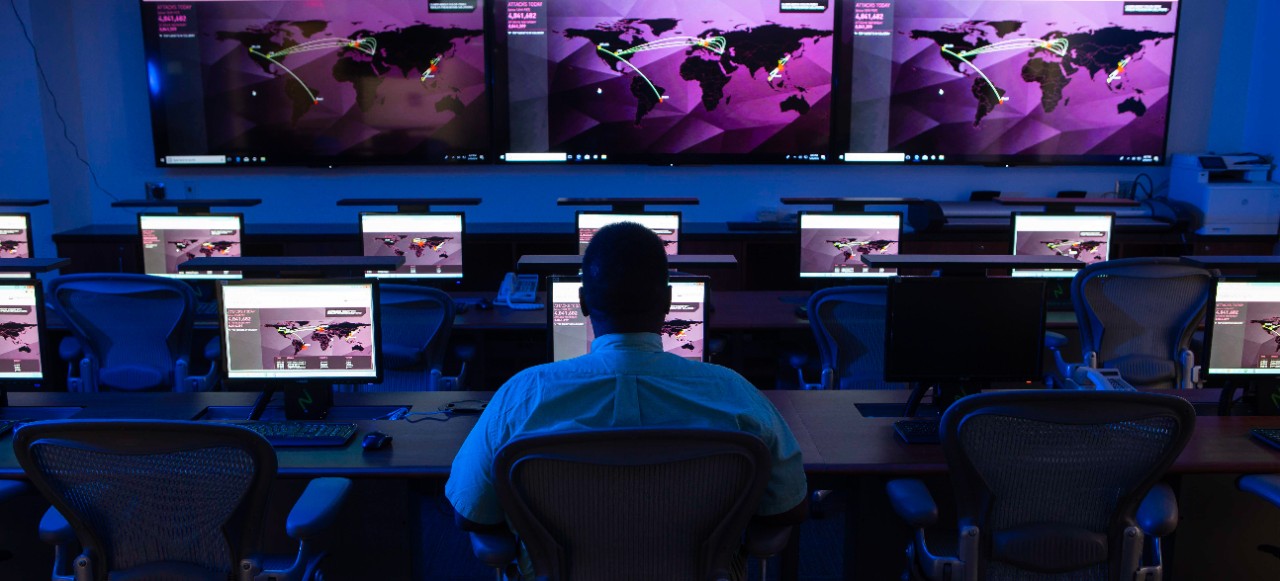 man in dark room with multiple computer screens in front of him 