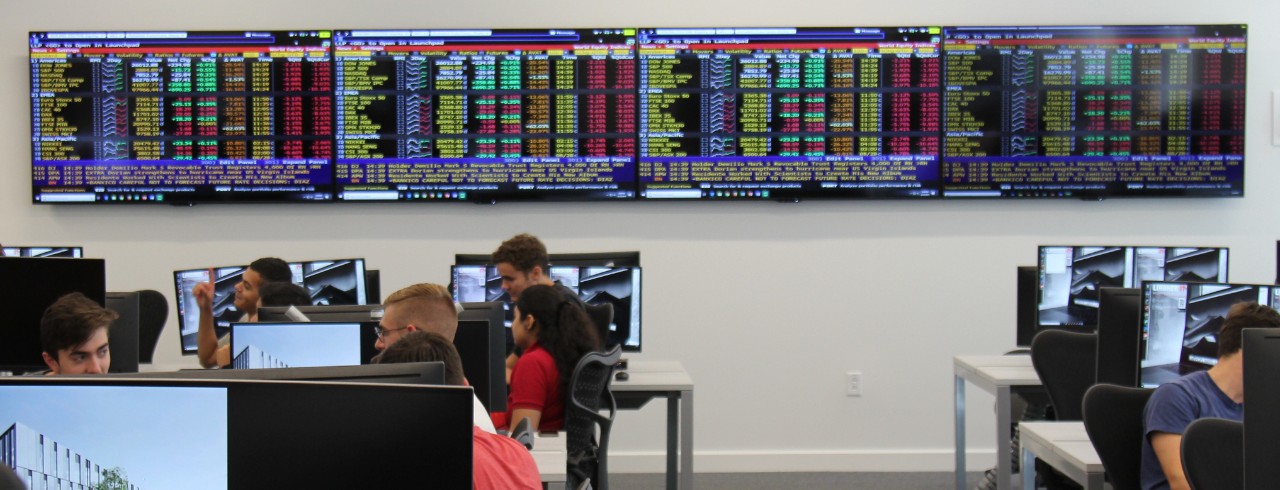 Students gather in Johnson Investment Lab at computer stations with stock market ticker on screens in the background